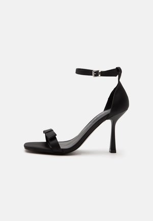 Black high-heeled sandal with an ankle strap, a silver buckle, and a front strap featuring a small bow detail.