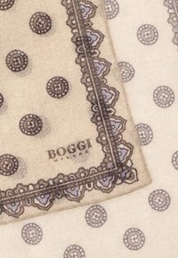 Beige scarf med intrikata mörkbruna kanter och cirkulära mönster. Materialet verkar mjukt med en texturerad finish. Varumärkeslogotyp synlig.