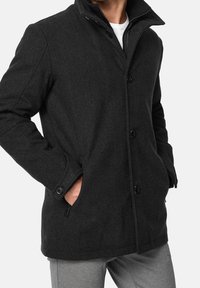 Black wool blend coat with a high collar, button front, and side pockets. Features textured fabric and a relaxed fit design.