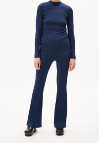 Top de manga larga con canalé en azul marino combinado con pantalones acampanados a juego, con un diseño ajustado y una textura suave. Usado con zuecos de plataforma negros.
