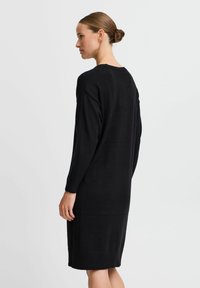 Abito nero a maglia con maniche lunghe, scollatura rotonda e dettagli a coste lungo i bordi, caratterizzato da una vestibilità dritta e morbida.