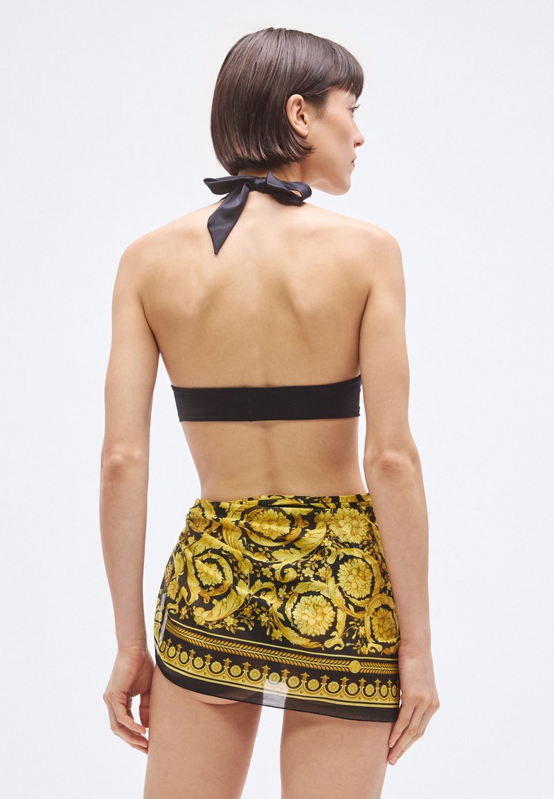 Black bandeau top with a back tie detail; paired with a patterned yellow and black wrap skirt featuring floral and baroque designs.