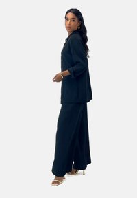 Zwart, textuurvol twee-delig outfit bestaande uit een loszittende, lange mouwen top en wijde broek, gecombineerd met lichtgekleurde, strap-heeled schoenen.