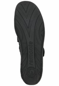 Semelle en caoutchouc noir avec une bande de roulement texturée et des motifs angulaires. Présente un logo circulaire et le nom de la marque embossés. Conception robuste et flexible.