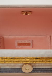 Pink interior of a purse featuring a gold metal snap closure, beige exterior, and a gold-tone brand label. Textured design with layered accents.