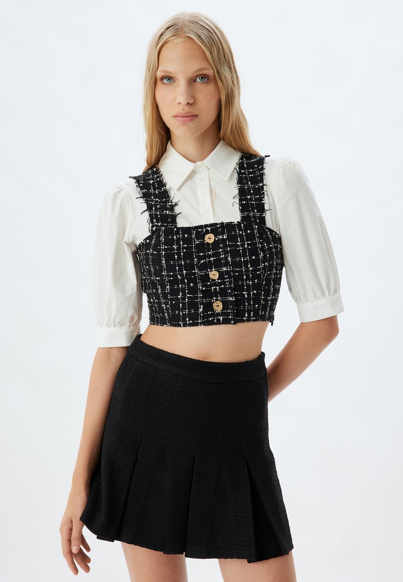 Zwart-witte geblokte crop top met knopen en rafelige banden, gecombineerd met een zwarte gestructureerde geplooide rok. Beide zijn op maat gemaakte pasvormen.