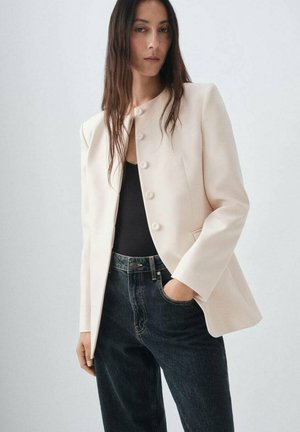 Blazer rose clair en tissu lisse, avec un col rond et six boutons assortis, associé à un jean taille haute en denim foncé.