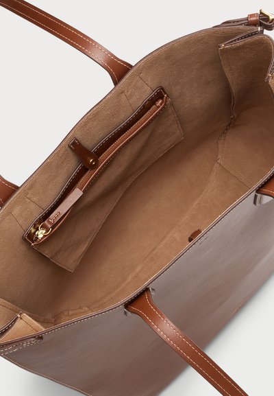 Interieur van een bruine leren tote bag, met een ritssluiting zak, een suède textuur en contrasterende tan voering. Inclusief insteekvakken en stevige handvatten.