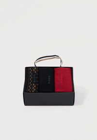 Drei Paar Socken in einer schwarzen Box: ein Paar mit einem gemusterten schwarz-gelben Design, ein einfarbiges schwarzes Paar und ein einfarbiges rotes Paar.