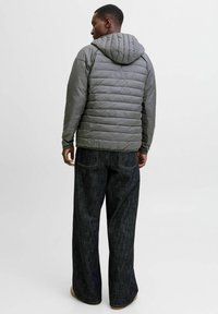 Gr�å pufferjakke med hætte, med stiftede paneler og en glat tekstur, parret med mørke, brede denimbukser.