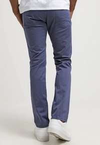 Blå bomullstwillbyxor med en figursydd design, med två bakfickor och rak benstruktur. Bärs med vita sneakers.