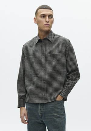Langærmet skjorte i sort og gråt ternet mønster med knaplukket krave, brystlommer og afslappet pasform. Båret med blå jeans.