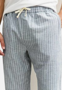 Pantalon rayé gris en tissu léger, avec une taille à cordon de serrage munie d'un lien couleur crème et des rayures blanches verticales pour la texture.