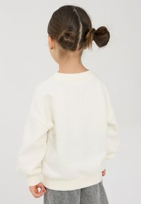 Biała bawełniana bluza z okrągłym dekoltem i opadłymi ramionami, z długimi rękawami i ściągaczem na dole. Widok z tyłu przedstawia minimalny design.