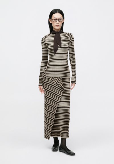 Vestido de malha riscada com mangas longas e detalhe de laço no pescoço. Tons terrosos de bege e castanho; silhueta ajustada com bainha assimétrica.