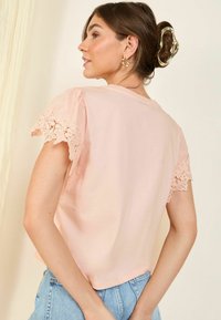 Haut rose clair à manches courtes avec des accents en dentelle sur les manches, en coton doux, coupe décontractée et encolure arrondie.
