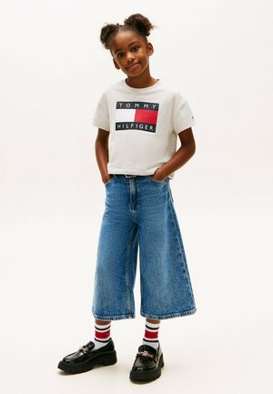 Grijze katoenen t-shirt met 'TOMMY HILFIGER' logo, wijdvallende blauwe denim culottes en zwarte loafers met kettingdetail. Gestreepte rode en witte sokken.