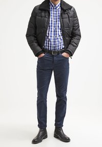 Zwarte gewatteerde jas met nepbont kraag, blauw en wit geruit overhemd, marineblauwe broek en zwarte leren laarzen. Casual gelaagd outfit.