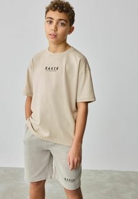 Beige tričko s krátkým rukávem s černým logem "BAKER", doplněné světle šedými šortkami se stejným logem. Měkká, jednoduchá látka z bavlny.