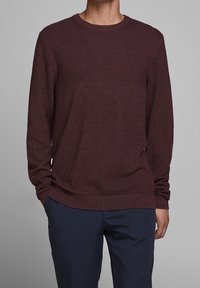 Bordowy sweter z dzianiny z długimi rękawami, zaokrąglonym dekoltem i teksturowanym wzorem; zestawiony z ciemnoniebieskimi spodniami dla kontrastu.