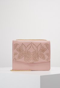 Borsa a pochette in pelle rosa con motivo floreale in borchie dorate e tracolla in oro, posizionata su un piedistallo bianco su uno sfondo neutro.