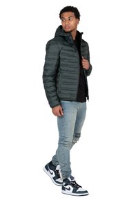 Giacca imbottita verde scuro con cappuccio, chiusura con zip e polsini a coste, abbinata a jeans skinny azzurri e sneakers in bianco e nero.