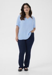 Blouse bleu clair, à manches courtes, avec un décolleté en V et une texture subtile, associée à un jean droit bleu foncé et des ballerines noires.