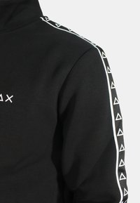 Felpa nera con colletto alto, caratterizzata da accenti a triangolo bianco lungo le maniche e un logo frontale bianco. Tessuto morbido.