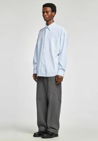 Jasnoniebieska koszula w paski z guzikiem z przodu i kieszenią, zestawiona z szarymi, szerokimi spodniami w paski i czarnymi butami.