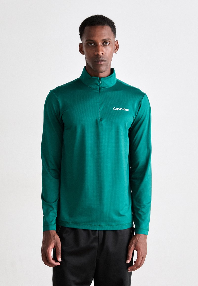 Pullover verde a maniche lunghe con mezza zip e colletto alto. Presenta il logo di Calvin Klein in bianco sul lato sinistro del petto. Tessuto morbido e leggero.