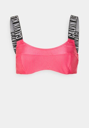 Roosa ribaga lühike topp laia musta rihmaga, millel on "CALVIN KLEIN" logo. Sujuv tekstuur, struktureeritud disain ja õmblusteta ääred.