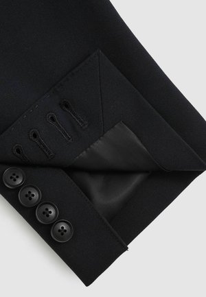 Svart skräddarsydd jackärm med ett glättat tyg, fyra svarta knappar och en sidentapet innerficka med dekorativ sömnad.
