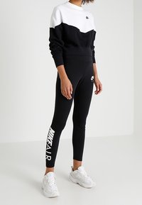 Svart och vit Nike sweatshirt med rund hals, tillsammans med svarta leggings som har "NIKE AIR" i vitt på sidan, och vita sneakers.