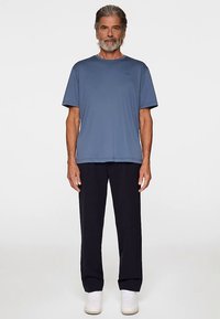 Blå kortärmad t-shirt med rund hals; kombinerad med marinblå byxor. Modellen bär vita skor. Enkel, avslappnad passform.