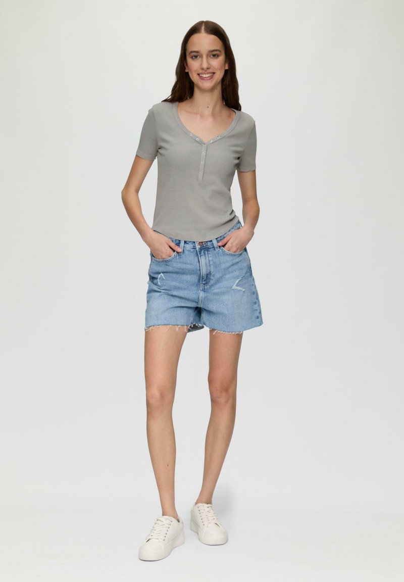 Grijs t-shirt met korte mouwen, een V-hals en knoopdetails, gecombineerd met lichtblauwe denim shorts met een rafelrand en zakken. Witte sneakers.