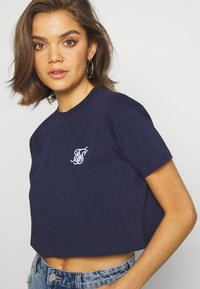 Camiseta de algodón de corte corto en azul marino con mangas cortas. Presenta un logo bordado en blanco en el pecho. Ajuste relajado y textura suave.