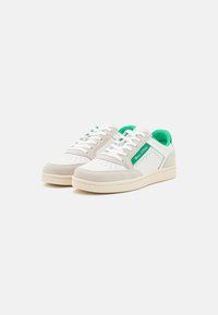 Białe i beżowe sneakersy z zielonymi akcentami, białymi sznurowadłami, perforowanymi detalami i zieloną metką "Marc O’Polo" z boku.