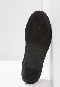 Svart gummisula med texturerat greppmönster, med varumärket "ANNA RIBELD" och storlek "37." Skon visas från botten i en vinkel.