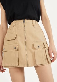 Kaki cargominikjol med dragkedja fram, sidfickor och en silverring som accent. Tjock bomullstyg med en slät textur.