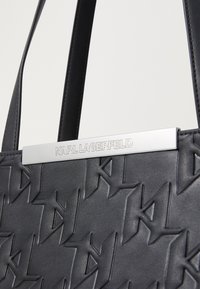 Borsa tote nera con superficie testurizzata e design del logo in rilievo. Gli accessori in argento nella parte superiore mostrano "KARL LAGERFELD."