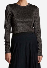 Svart långärmad topp med en metallisk, glittrig textur; rund hals; figurnära design som matchas med en plisserad svart kjol.