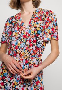 Floral dress featuring a V-neckline and short sleeves. Made of lightweight fabric with a vibrant multicolor flower pattern and elastic waist.