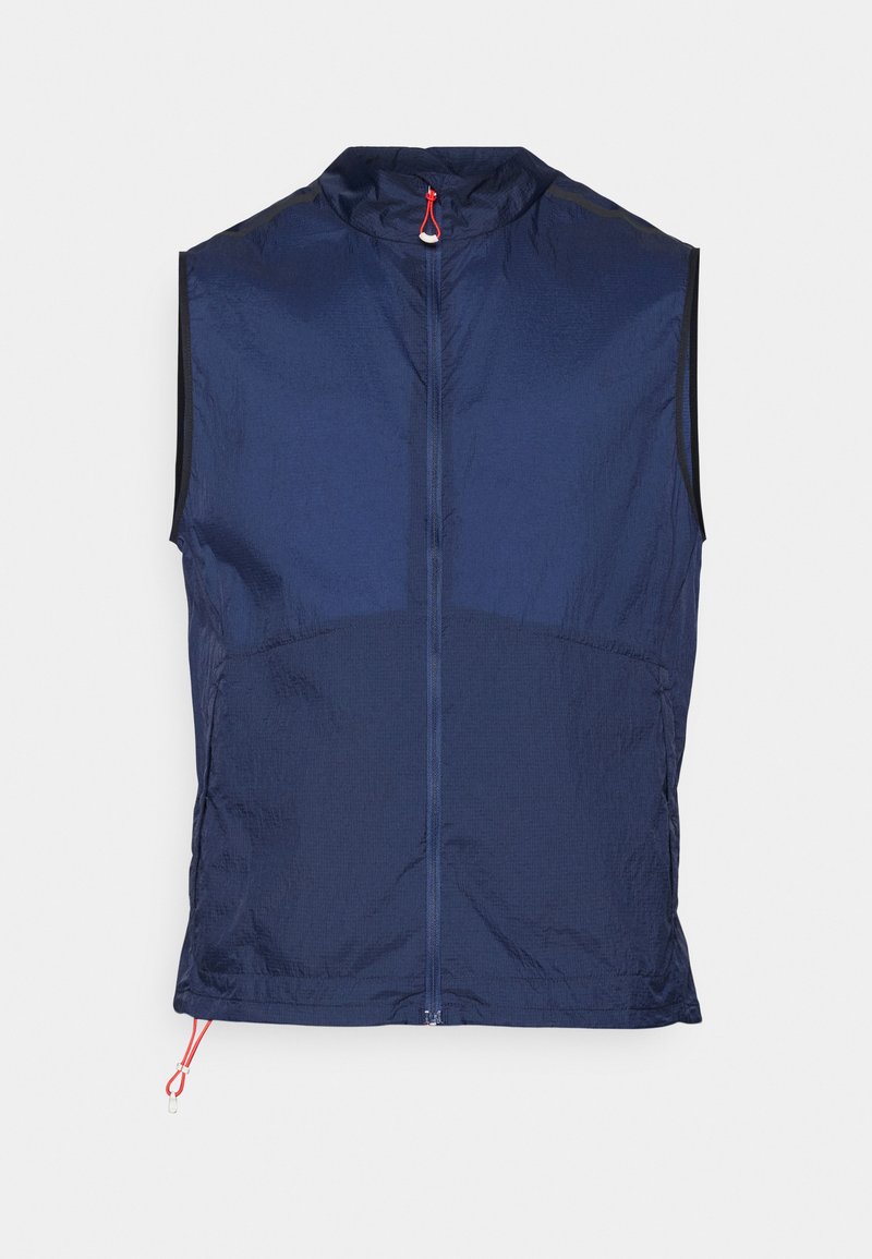 Gilet sans manches bleu marine en tissu léger, avec un col haut, une fermeture éclair sur toute la longueur à l'avant et des accents en cordon rouge au bas.