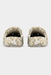 Πλάγια όψη μπεζ και λευκών κλογκ με μοτίβο παραλλαγής, με οπές αερισμού και ρυθμιζόμενα λουράκια στη φτέρνα.