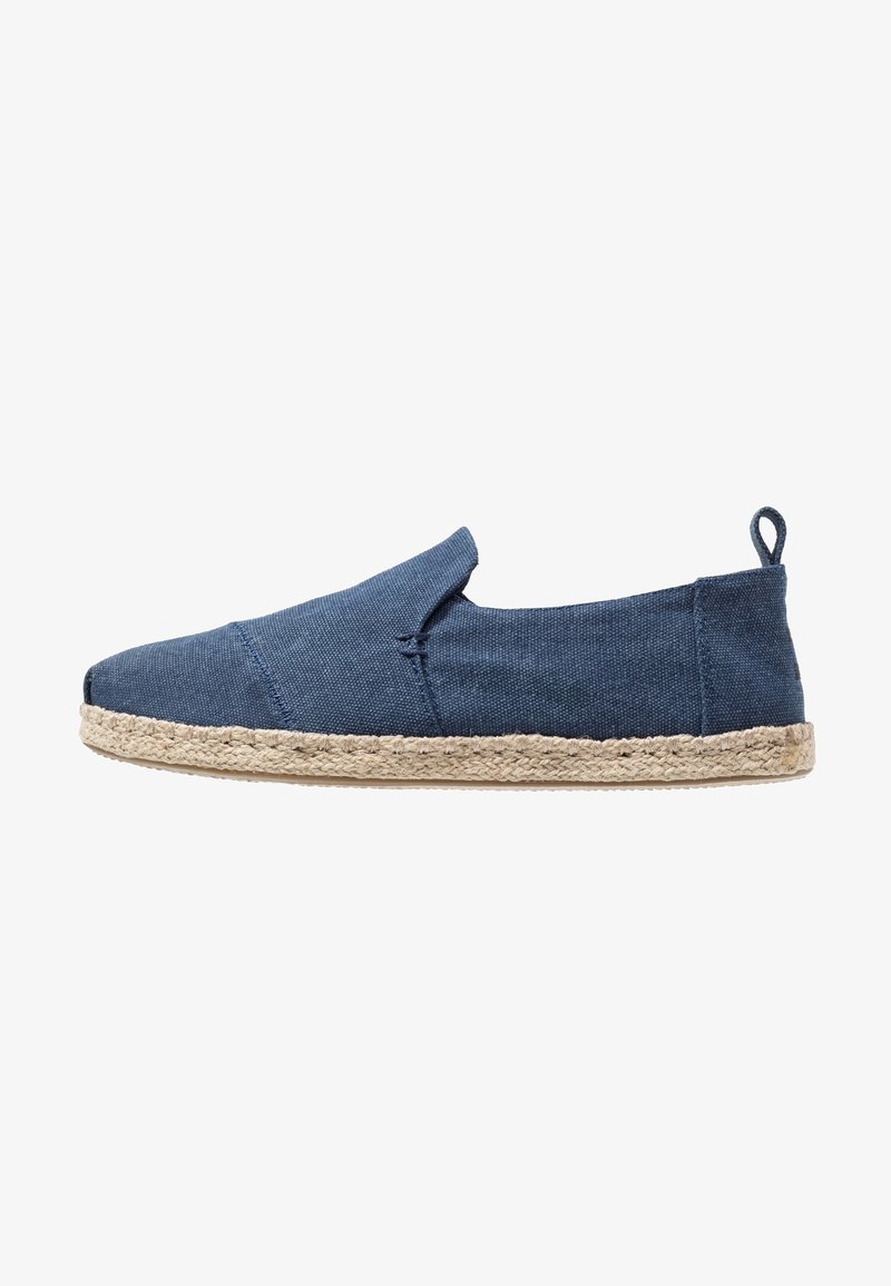 Chaussure à enfiler en toile bleue avec semelle en corde de jute, présentant un bout arrondi et un élastique latéral pour un enfilage facile. Design minimaliste avec des détails cousus.