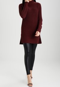 Burgundy stickad tunika med ribbad textur och sidofickor, tillsammans med svarta faux läderleggings och svarta remsandaler.