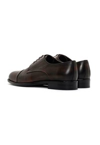 Zapatos de vestir de cuero marrón con una textura suave, punta redondeada, diseño con cordones y tacón bajo negro, que presentan detalles de costura sutiles.