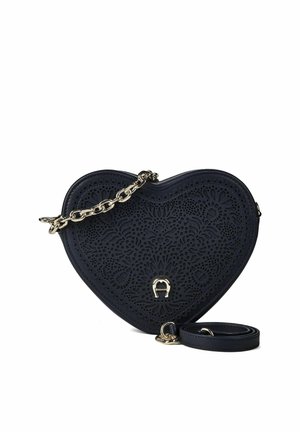 Herzförmige dunkelblaue Handtasche mit filigranen, laser ausgeschnittenen Blumenmustern und goldenem Kettenriemen auf weißem Hintergrund.