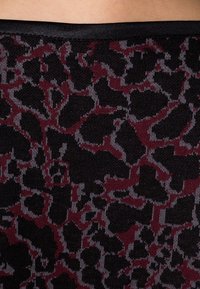 Tejido de punto con un fondo negro que presenta un patrón de estampado de leopardo en tonos burdeos y gris. Textura suave, terminado con un ribete negro.