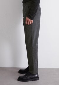 Pantaloni grigi su misura in tessuto tessuto, con vestibilità aderente e tasche laterali, abbinati a scarpe nere con lacci.